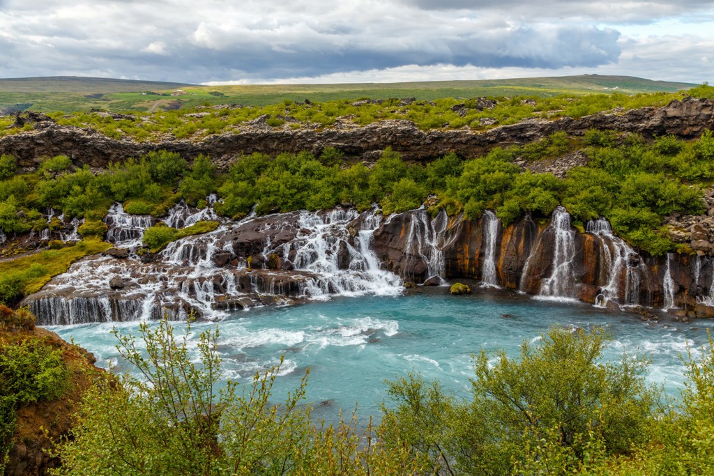 Waterval met helderblauw rivierwater en groene begroeiing in IJsland tijdens een groepsrondreis.