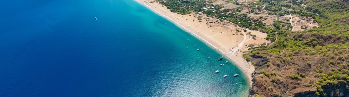 het strand en de baai van Olympos bij Antalya, met turquoise zee en bergen op de achtergrond.