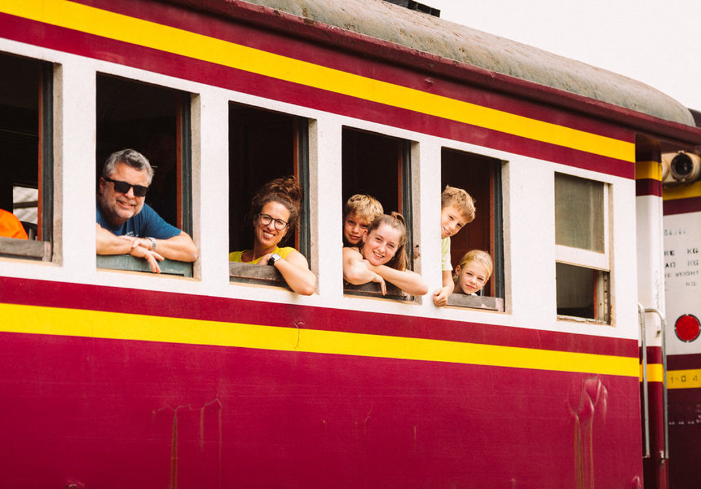 Gezin kijkt uit het raam van een kleurrijke trein tijdens familiereis Thailand, route van 15 dagen.