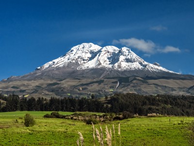 Besneeuwde Cotopaxi-vulkaan in Ecuador met groene velden op de voorgrond.