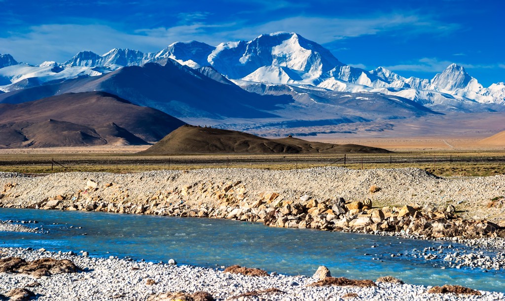 Besneeuwde bergtoppen in Tibet met rivier op de voorgrond, tijdens groepsrondreis Tibet en Nepal.