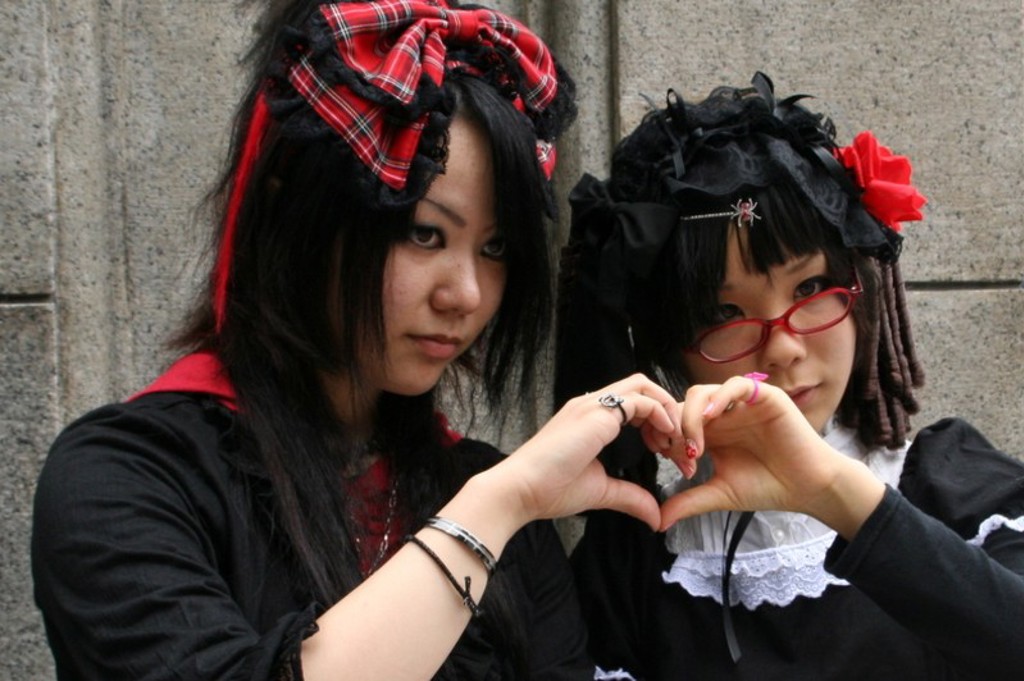 Twee jongeren in Japanse streetfashion vormen een hartje met hun handen tijdens een familiereis Japan.