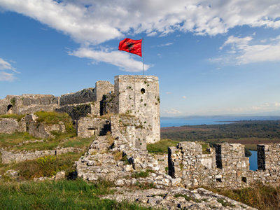 Kasteelruïne in Albanië met wapperende Albanese vlag en uitzicht op het landschap en water.