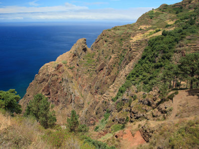 Uitzicht op de ruige kustkliffen van Madeira met blauwe oceaan en wandelpad langs de berghelling.