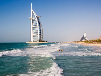 Burj Al Arab aan het strand van Dubai, met golven en de skyline op de achtergrond.