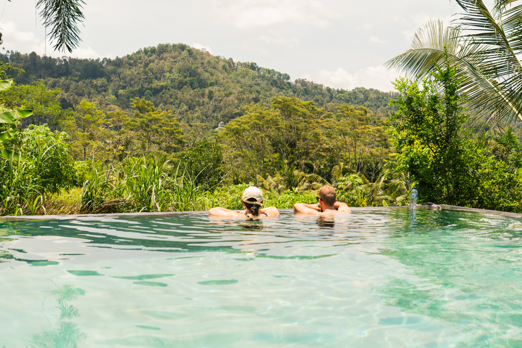 Twee reizigers ontspannen in een infinitypool met uitzicht op de groene jungle van Indonesië.