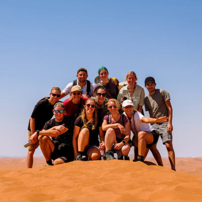 Groep 22-35ers op zandduin tijdens rondreis door Zuidelijk Afrika.