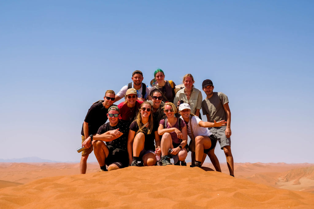 Groep 22-35ers op zandduin tijdens rondreis door Zuidelijk Afrika.