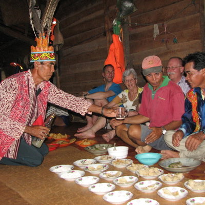Lokale gastheer in traditionele kleding schenkt drank tijdens bezoek aan een longhouse op Maleisisch Borneo.