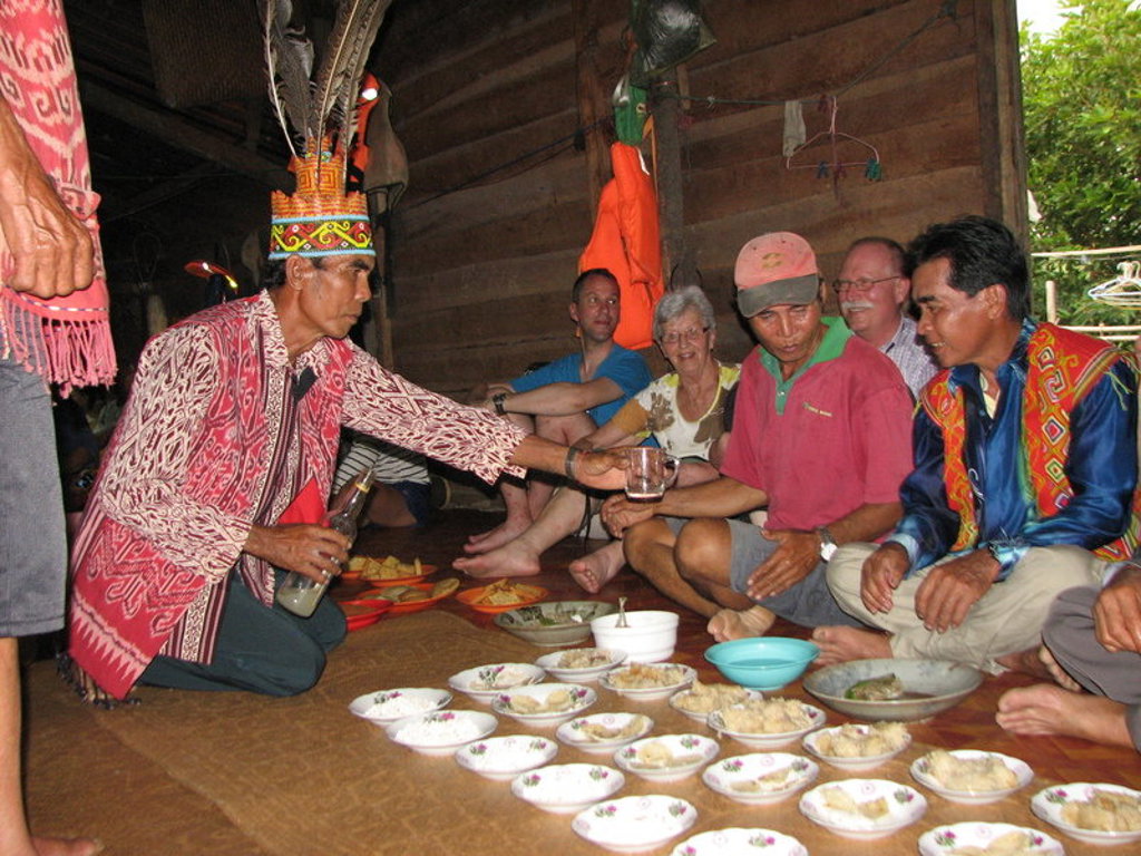 Lokale gastheer in traditionele kleding schenkt drank tijdens bezoek aan een longhouse op Maleisisch Borneo.