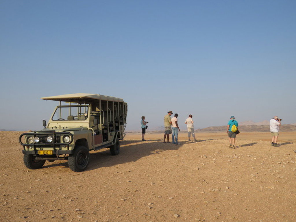 Safariwagen met reizigers tijdens groepsrondreis in Namibië, met woestijnlandschap op de achtergrond.