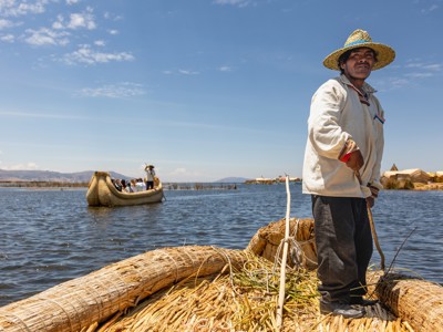 Man op rieten boot op het Titicacameer bij de drijvende Uros-eilanden, Route Peru.