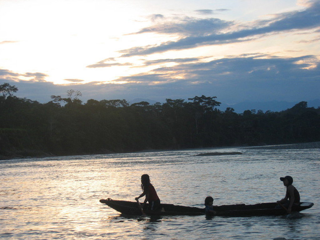 Kano met drie personen op een rivier bij zonsondergang in Ecuador.