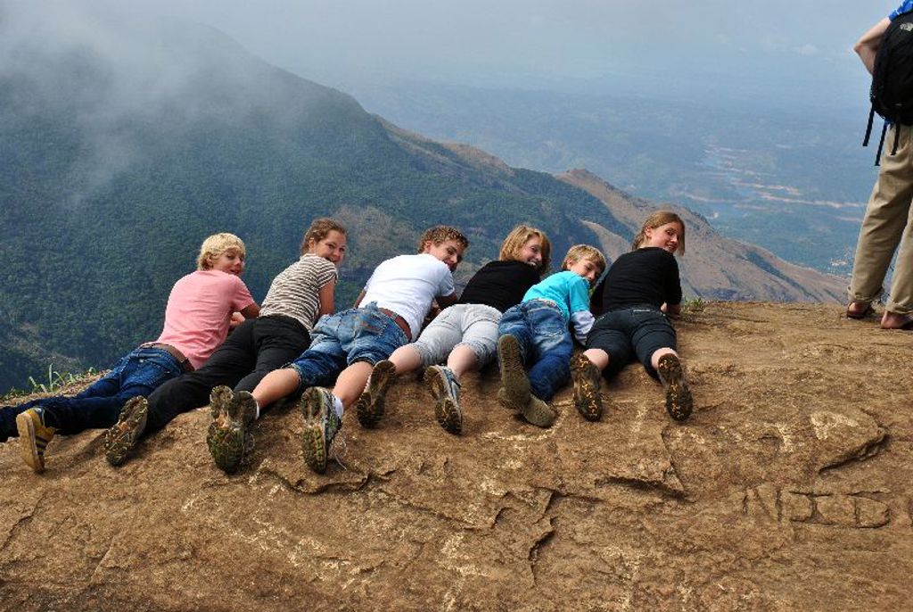 Kinderen liggen op een rotsplateau met uitzicht op bergen tijdens een familiereis in Sri Lanka.