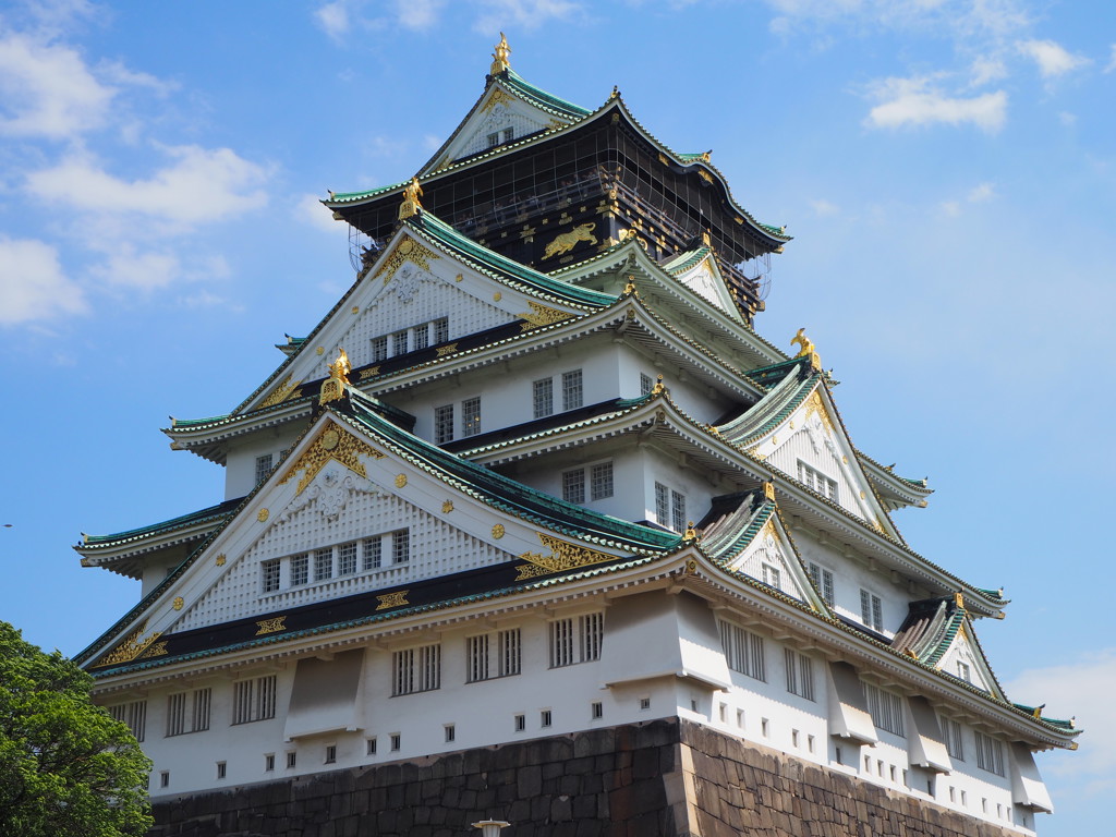Osaka Castle in Japan met groene daken en gouden details onder een blauwe lucht.