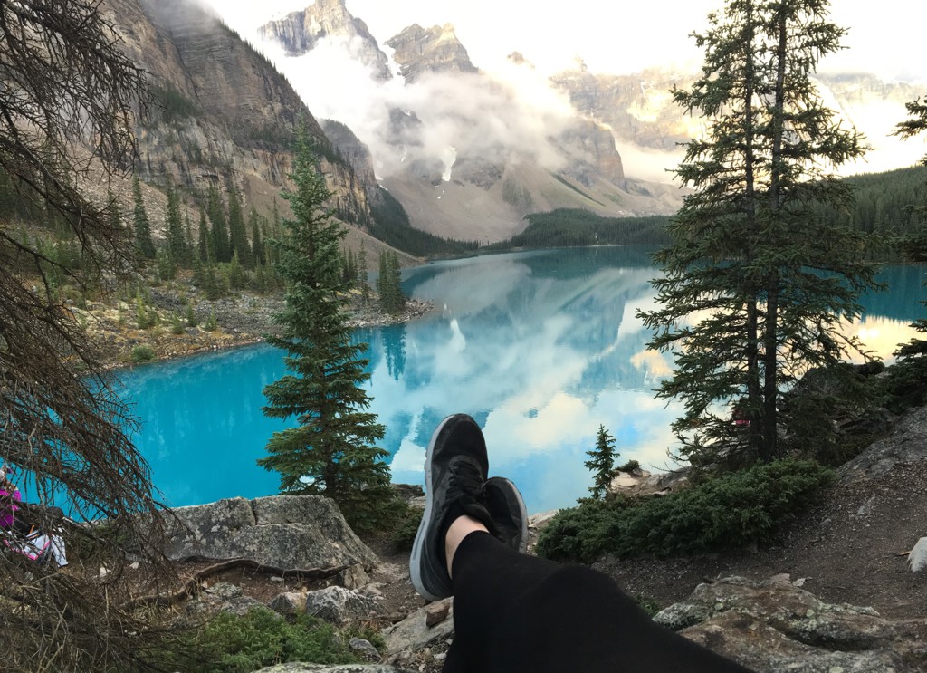 Uitzicht over een turquoise bergmeer in Canada West, met dennenbomen en besneeuwde bergtoppen.
