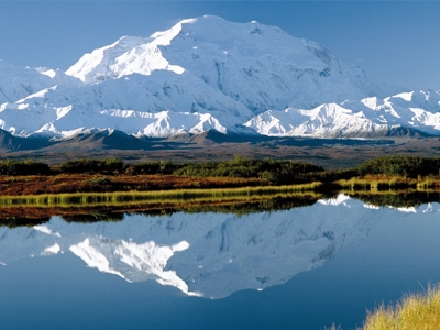 Besneeuwde bergtop in Alaska weerspiegeld in een rustig meer langs de Route Alaska.