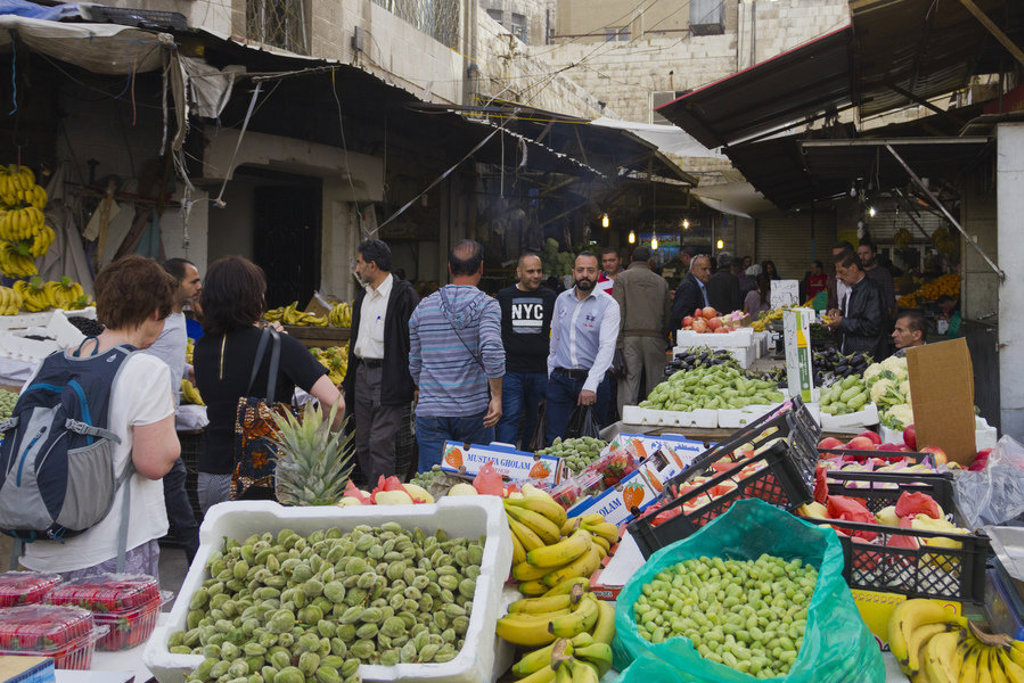 Drukke markt in Jordanië met fruit- en groentekraampjes en reizigers tussen de kramen.