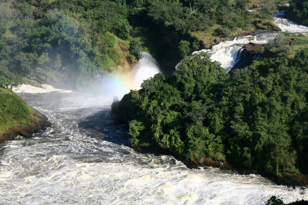 Waterval in groen regenwoud in Oeganda, met nevel en regenboog boven de rivier.