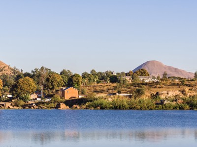 Uitzicht op dorp aan een meer in Madagascar met heuvels op de achtergrond.