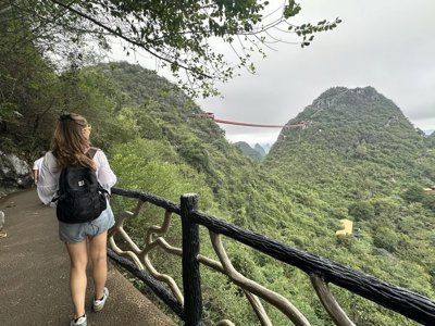 Wandelen over bergpad met uitzicht op een hangbrug tussen groene bergen tijdens groepsrondreis China.