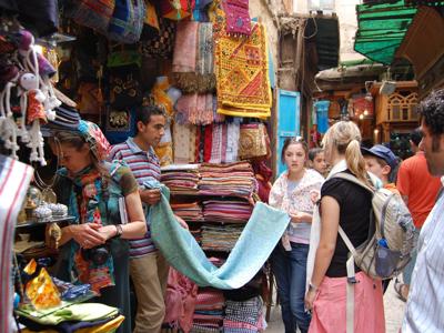 Drukke bazaar in Egypte met reizigers die kleurrijke stoffen en souvenirs bekijken.