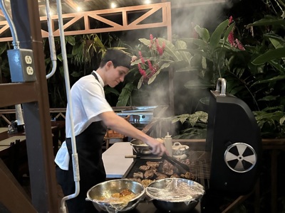 Kok bereidt vlees op de barbecue tijdens Route Costa Rica, in een overdekte buitenkeuken.
