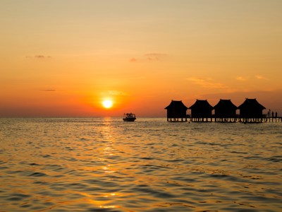 Zonsondergang boven zee met boot en paalwoningen op een pier tijdens de route Kalimantan.