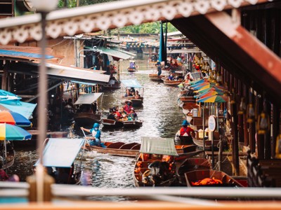 Drijvende markt in Thailand met longtailboten en kleurrijke parasols langs een kanaal.