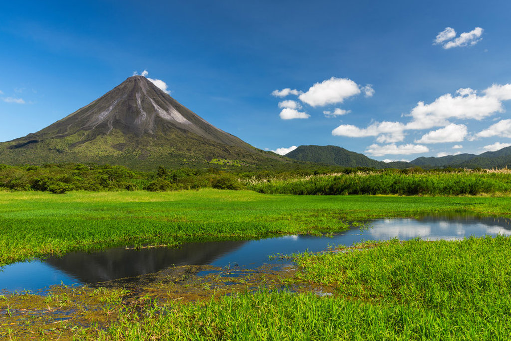 Vulkaan Arenal in Costa Rica met groen landschap en waterpartij onder een blauwe lucht.