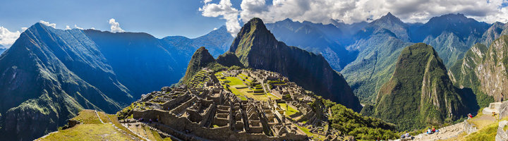 Panorama van Machu Picchu in Peru, omringd door groene Andesbergen onder een blauwe lucht.