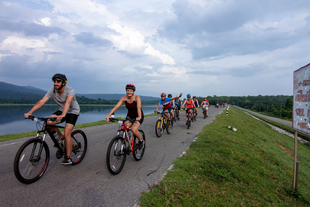 Groep fietsers tijdens fietsvakantie in Vietnam, Cambodja en Thailand langs een meer over een dijkweg.