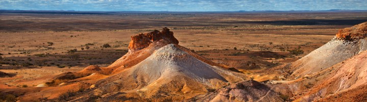 Roodkleurig woestijnlandschap met opaalmijnheuvels bij Coober Pedy in Australië, onder een wolkenlucht.