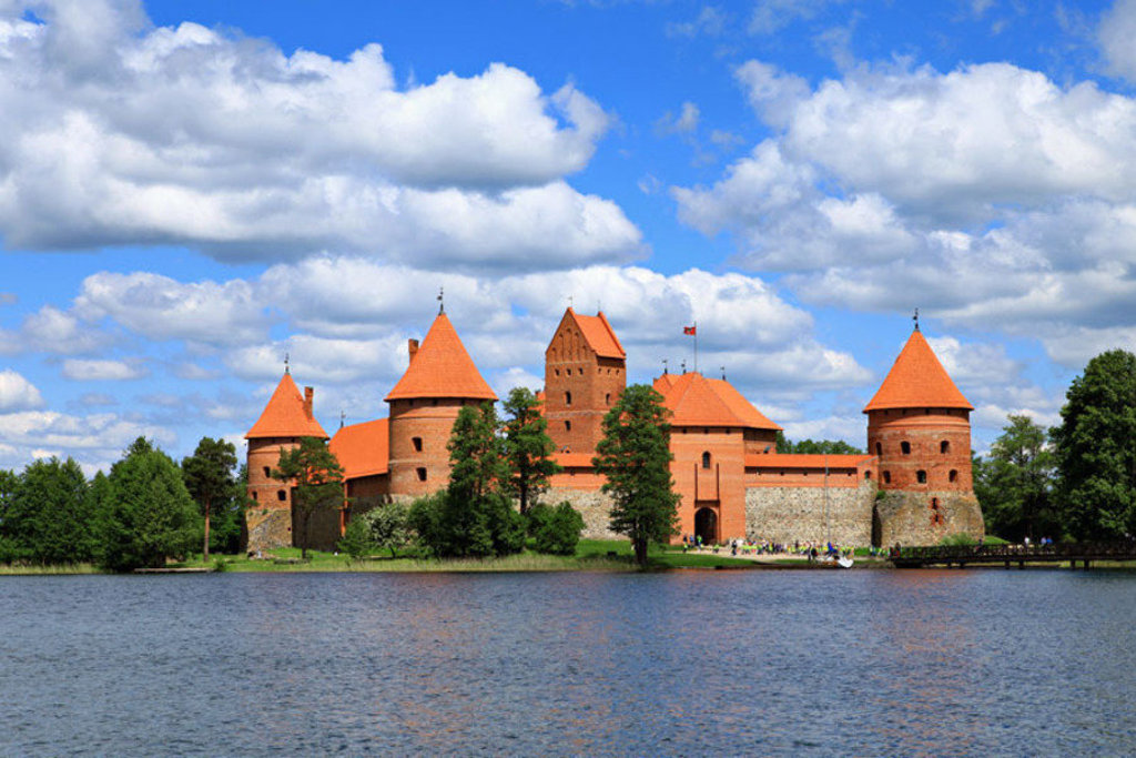 Trakai-kasteel in Litouwen aan een meer, met rode torens en blauwe lucht met wolken.
