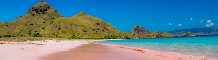 Roze zandstrand van Pink Beach op Komodo, met turquoise zee en groene heuvels op de achtergrond.