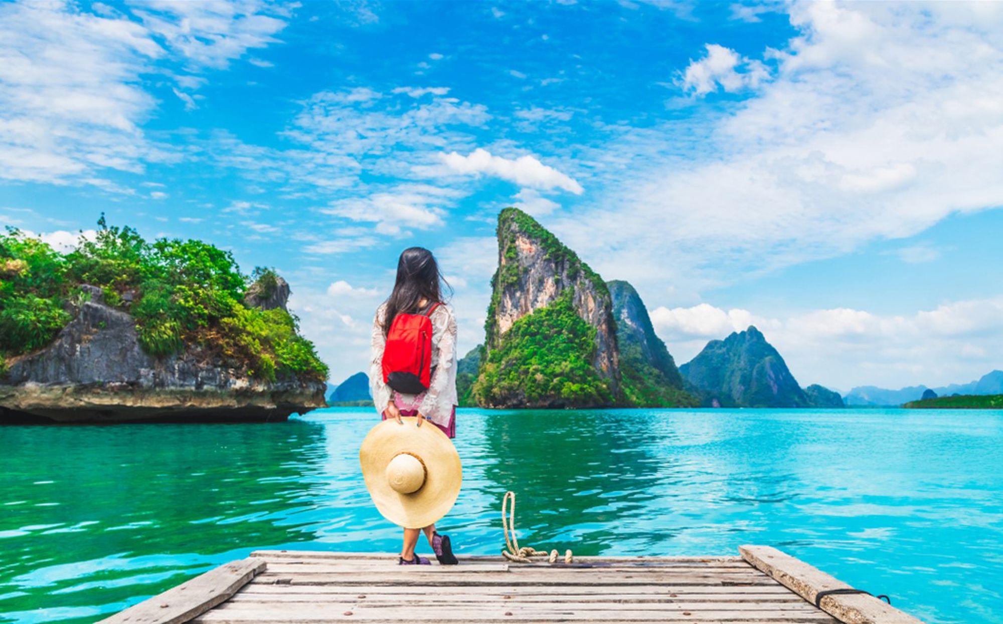 Reiziger op houten steiger kijkt uit over turkoois water en kalksteenrotsen in Thailand.