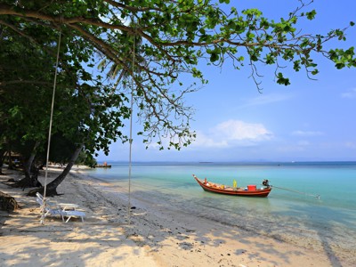 Tropisch strand in Thailand met schommel aan een boom en longtailboot in helderblauw water.