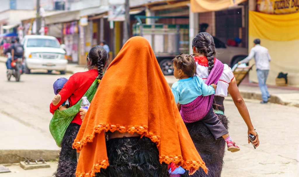 Vrouwen met kinderen in draagdoeken lopen door een straat in Mexico tijdens een groepsrondreis.