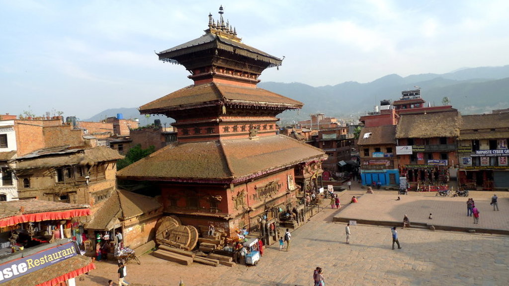Plein met traditionele tempel in Kathmandu, Nepal, met omringende gebouwen en bergen op de achtergrond.