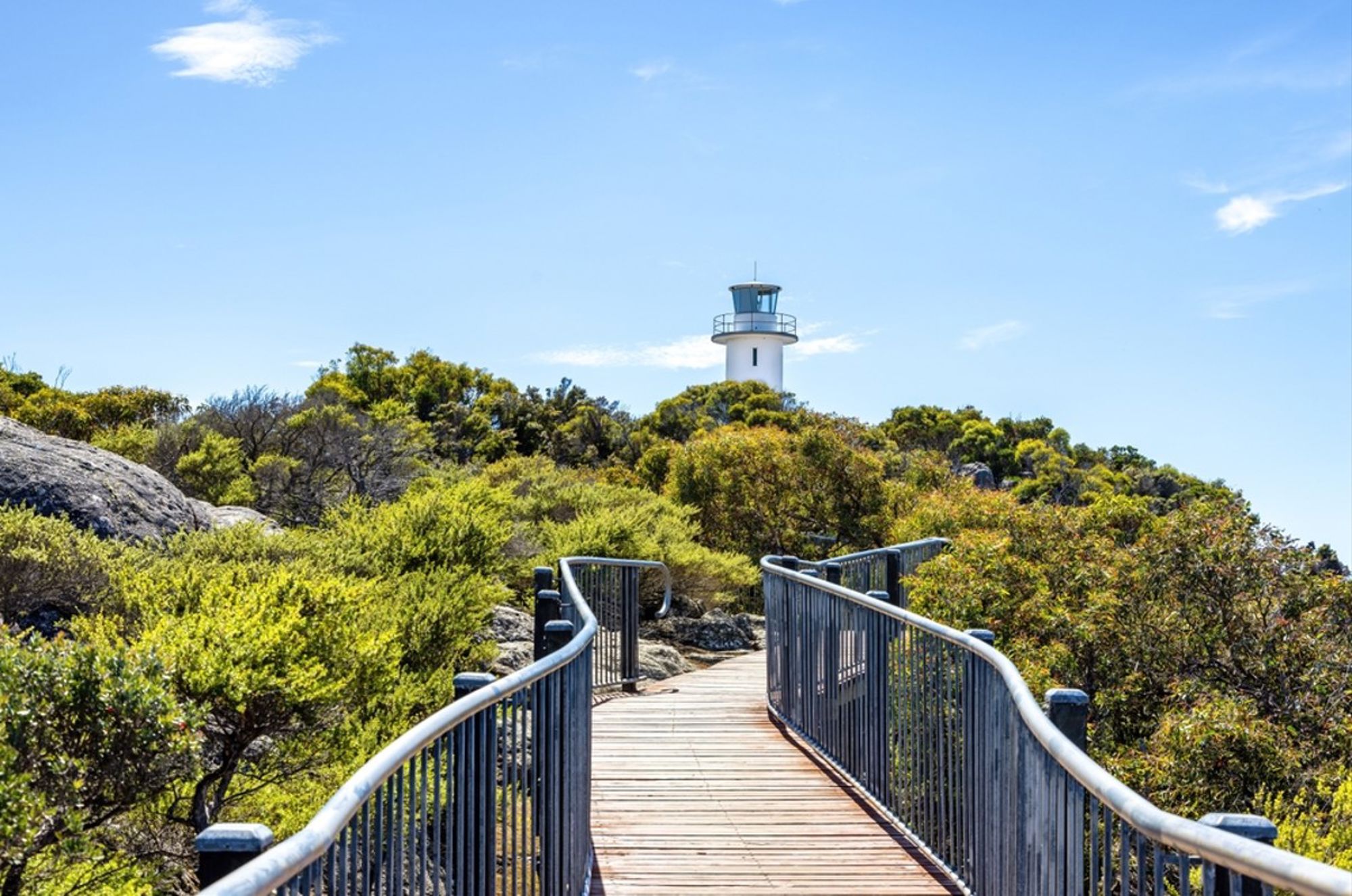 Wandelpad met uitzicht op een vuurtoren tussen groen struikgewas in Australië.