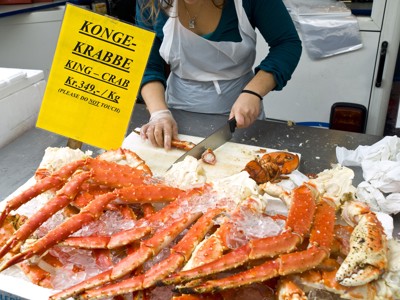 Verse koningskrab op ijs op een vismarkt in Scandinavië, met verkoper die de krab klaarmaakt.