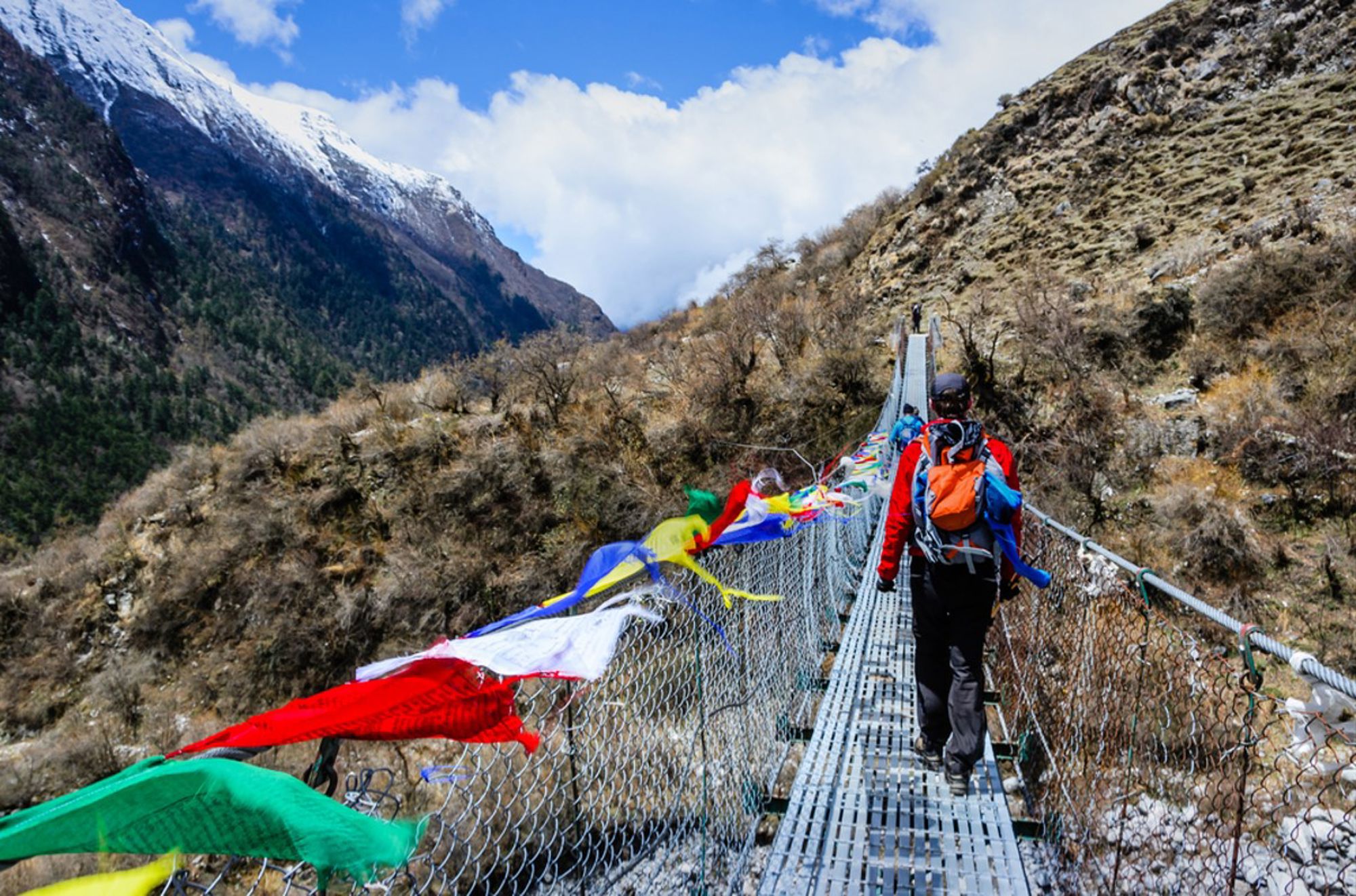 Wandelaar op hangbrug met gebedsvlaggen tijdens een trekking in de Nepalese Himalaya.