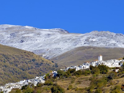 Wit bergdorp in de Alpujarras met besneeuwde Sierra Nevada op de achtergrond, Andalusië.