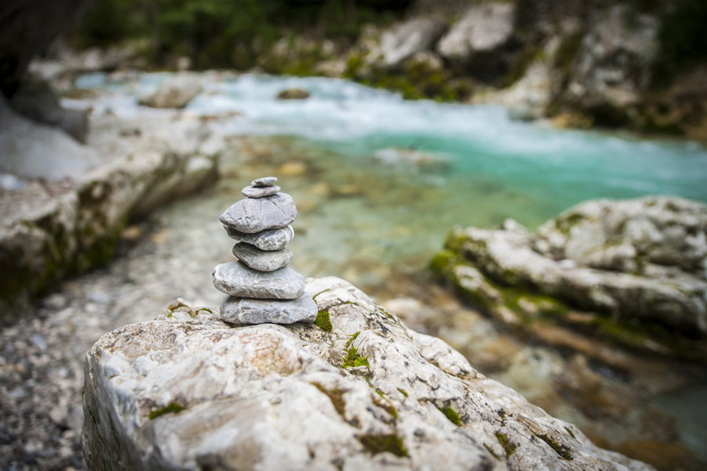 Gestapelde stenen op een rots bij een helderblauwe rivier in Slovenië, tijdens een 22-35ers reis.
