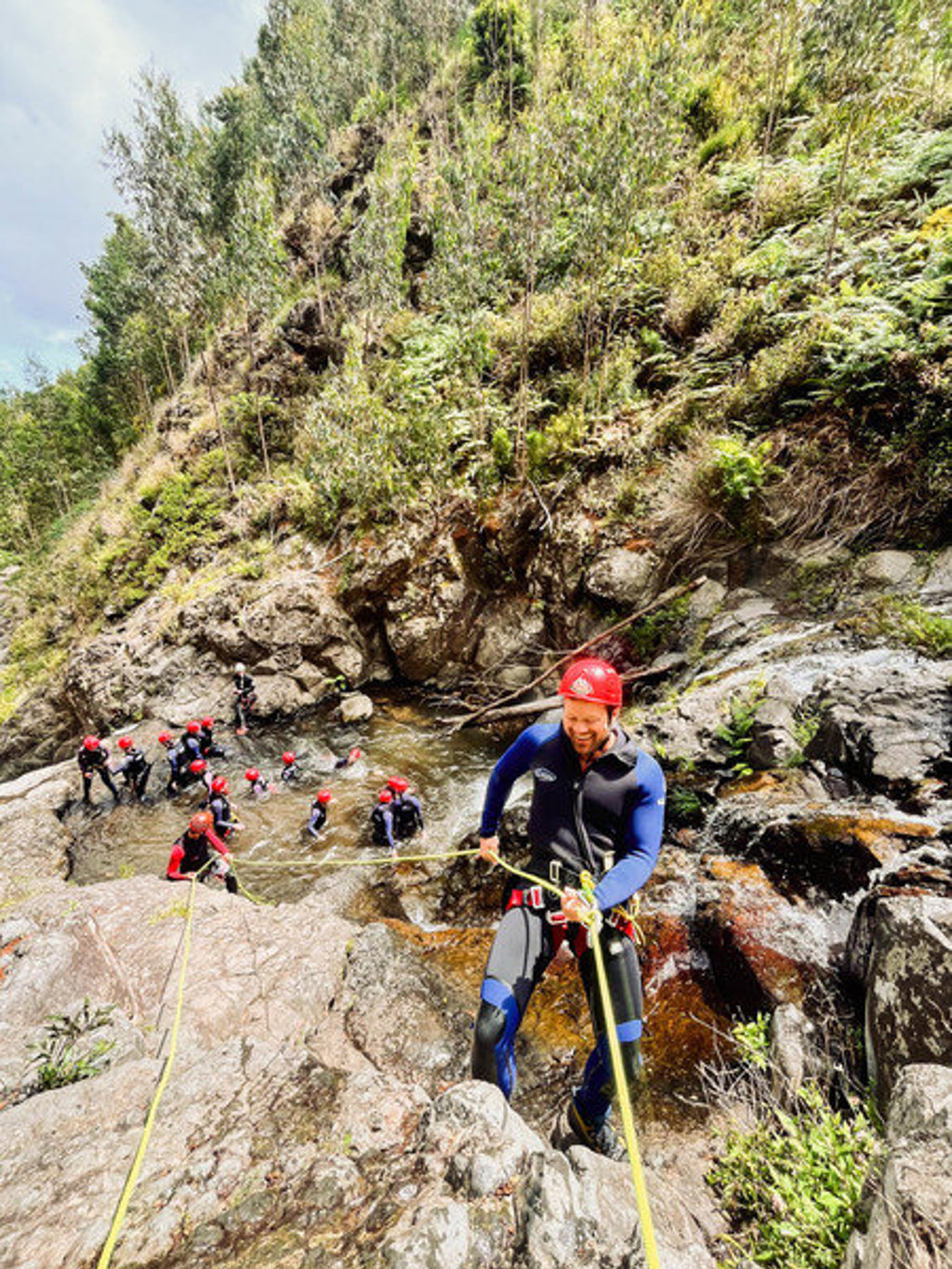 Canyoning op Madeira: reiziger klimt met touw langs rotsen, groep in wetsuits en helmen in de rivier.