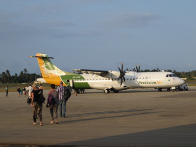 Reizigers lopen over het platform naar een Precision Air-vliegtuig tijdens de route Kenia, Tanzania en Zanzibar.