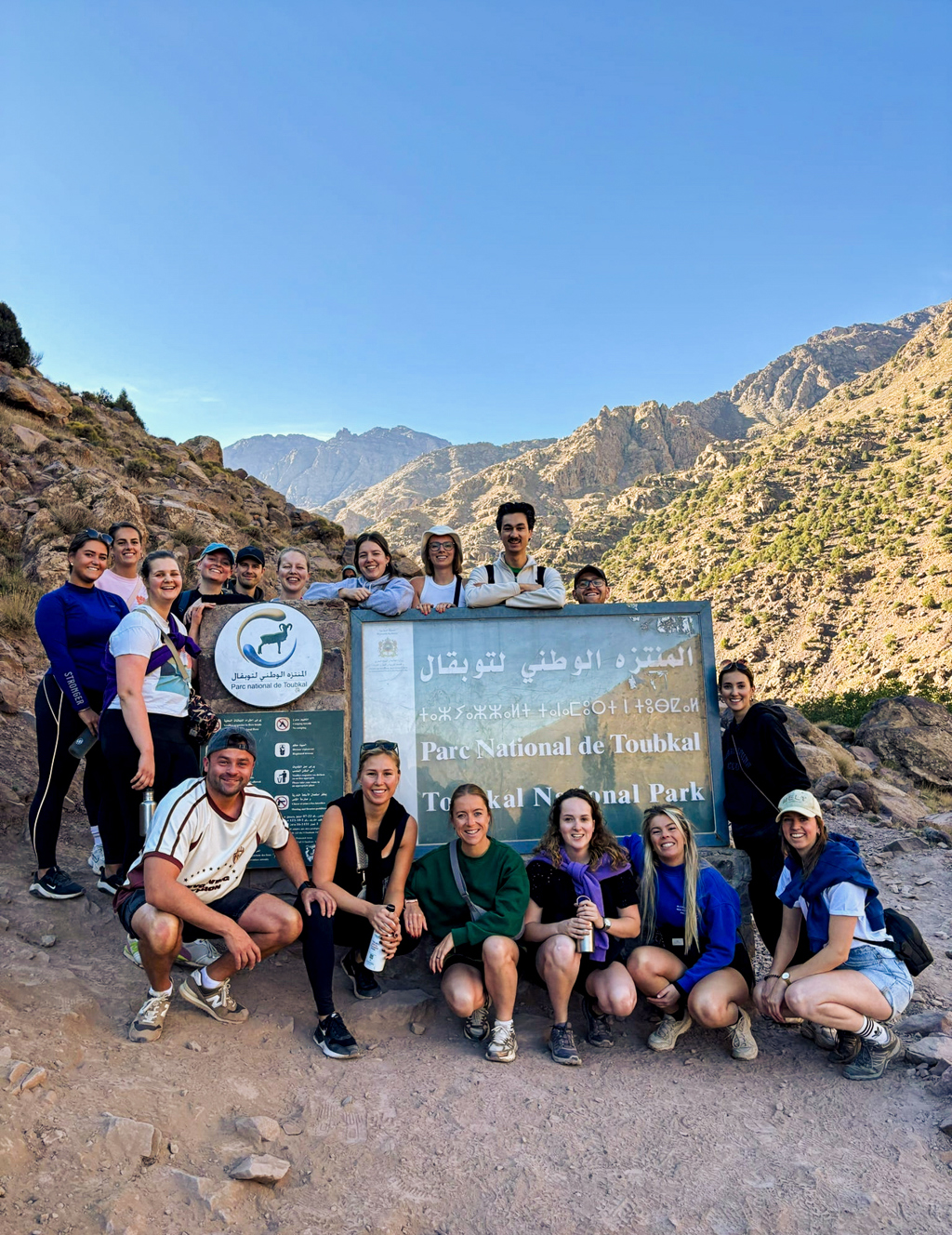 Groep 22-35ers reizigers bij het bord van Parc National de Toubkal in het Atlasgebergte, Marokko.