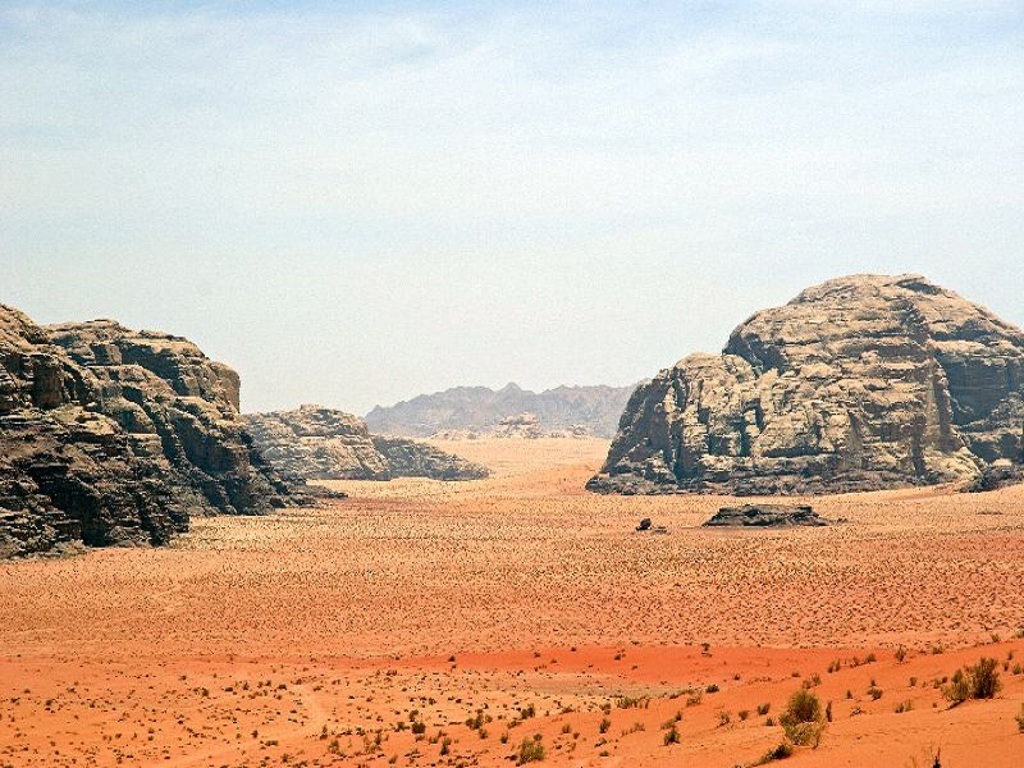 Wadi Rum-woestijn in Jordanië met rood zand en rotsformaties onder een heldere lucht.