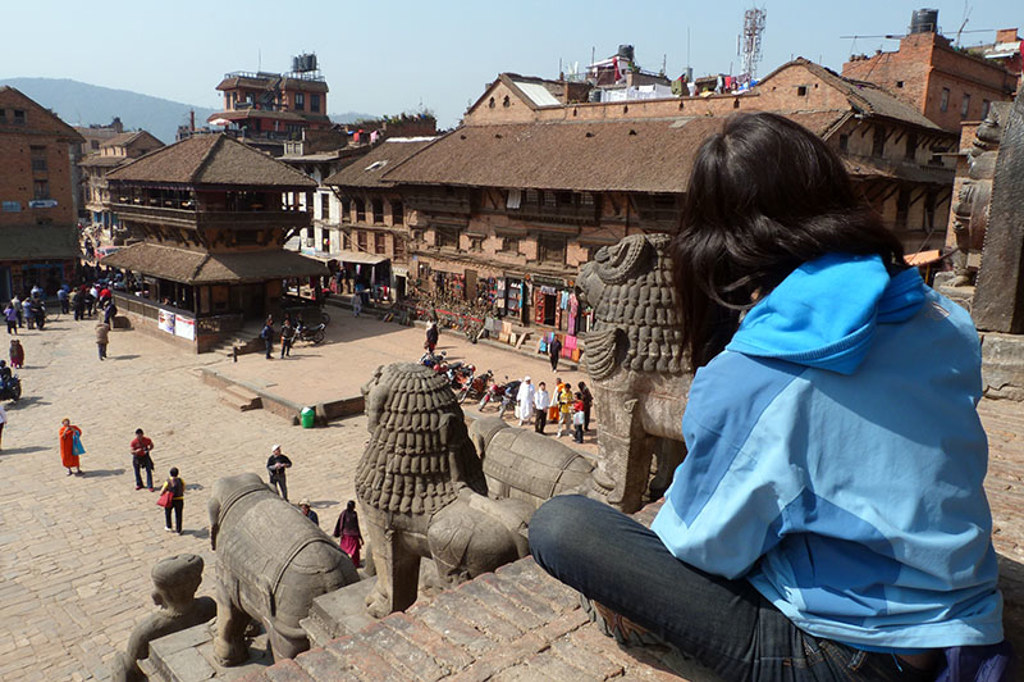 Uitzicht over Durbar Square in Bhaktapur, Nepal, met tempelwachters en reiziger op traptreden.