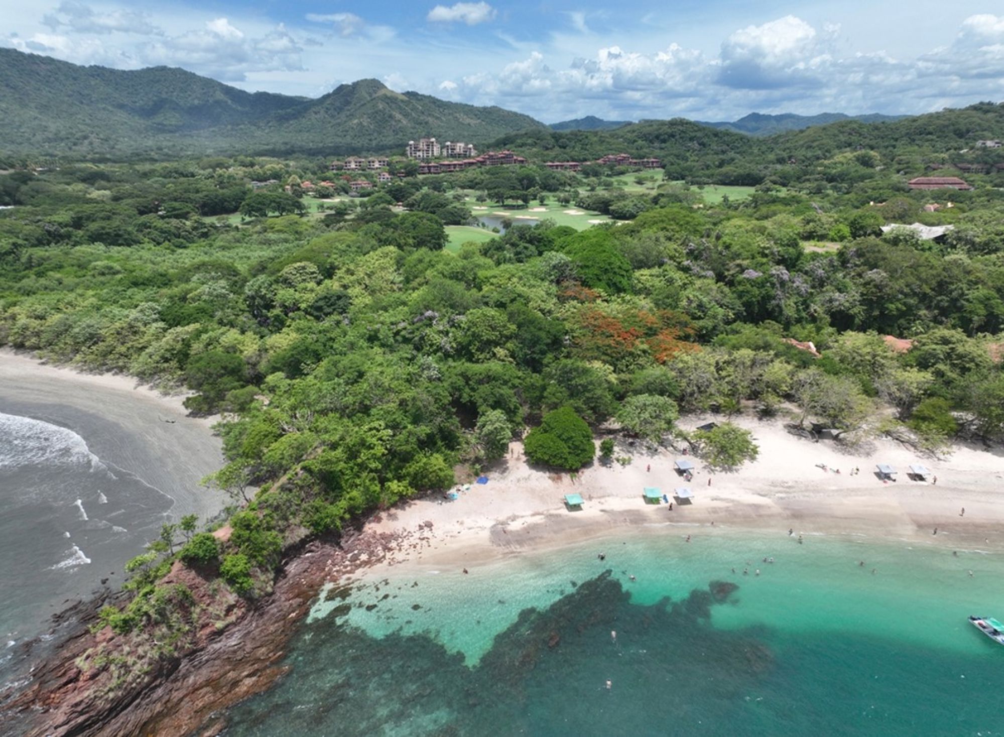 een strand in Costa Rica met turquoise zee, groen tropisch bos en bergen op de achtergrond.